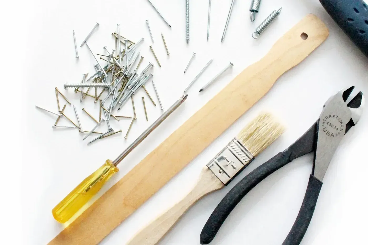 Handyman tools laid out: nails, screwdriver, paintbrush, and pliers